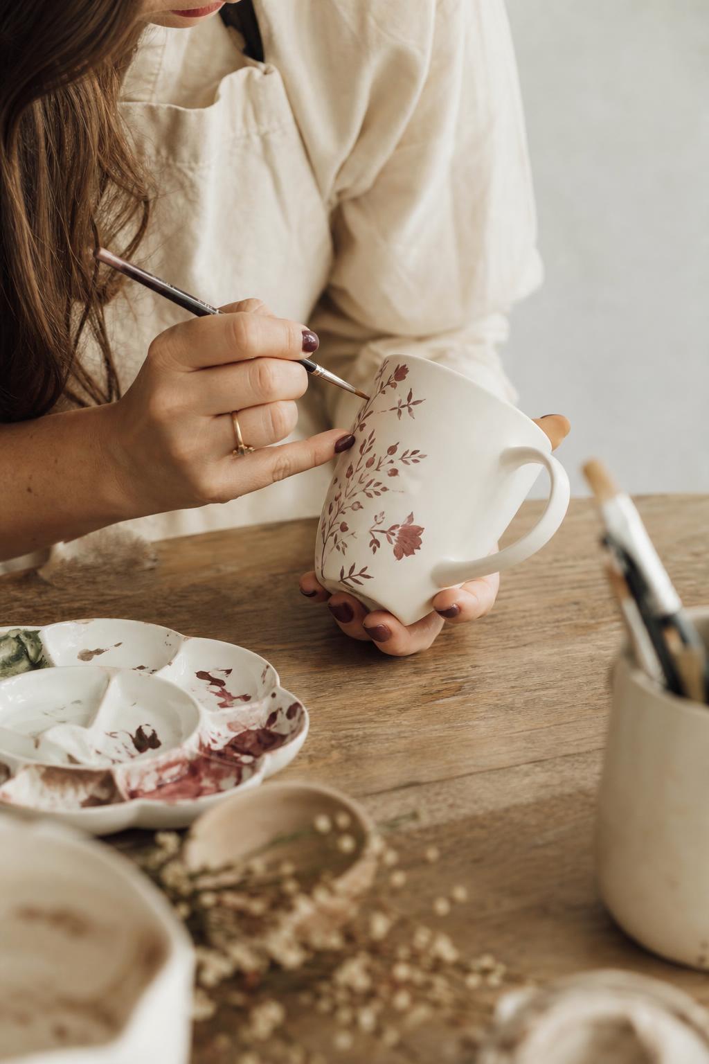 Mãos pintando uma caneca de cerâmica com pincel fino